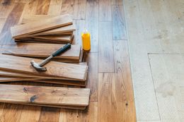 A hammer and a bottle of glue are sitting on a wooden floor.