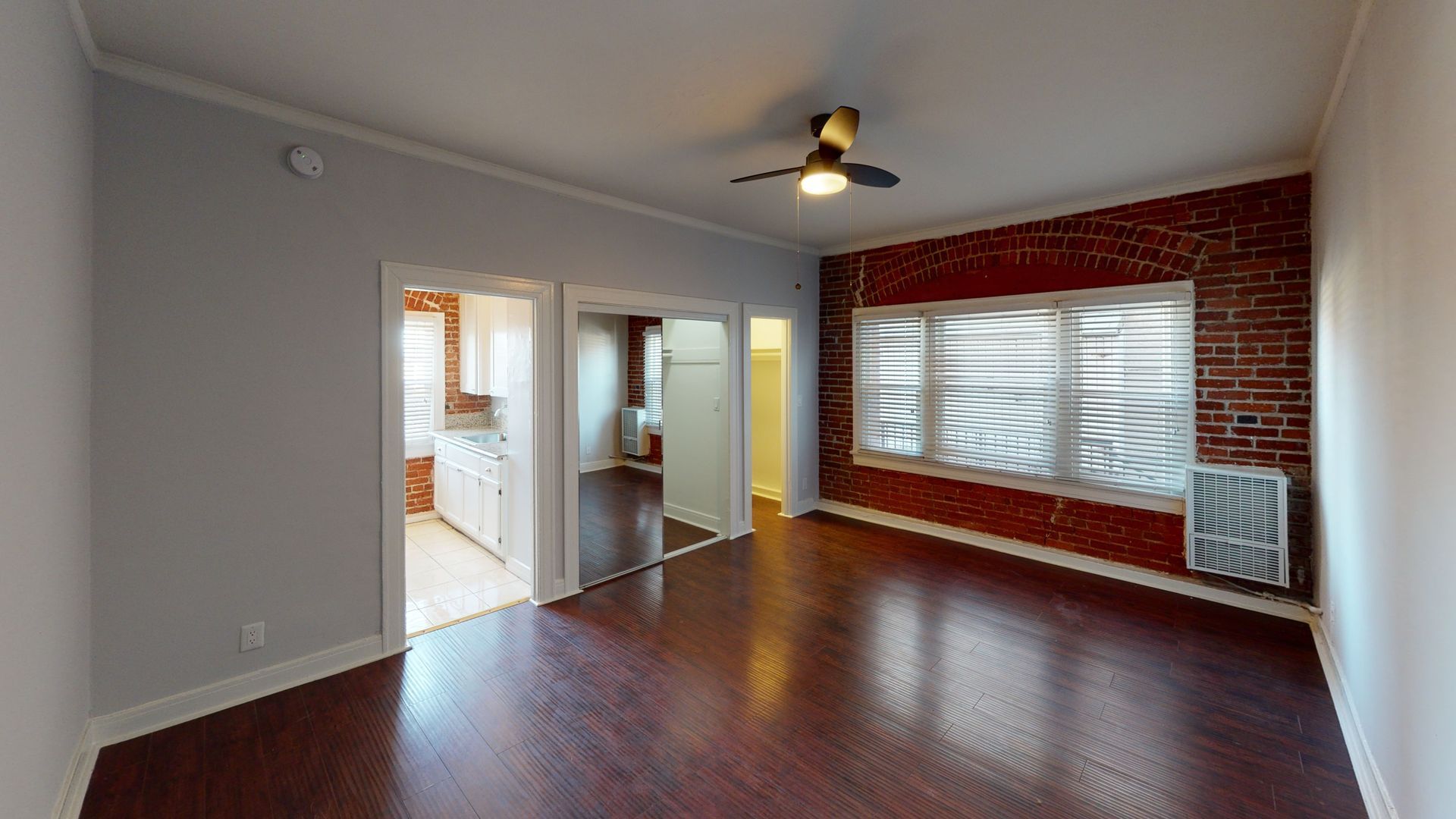 Living room with dark wood floors, exposed brick wall, and doorways to other rooms.