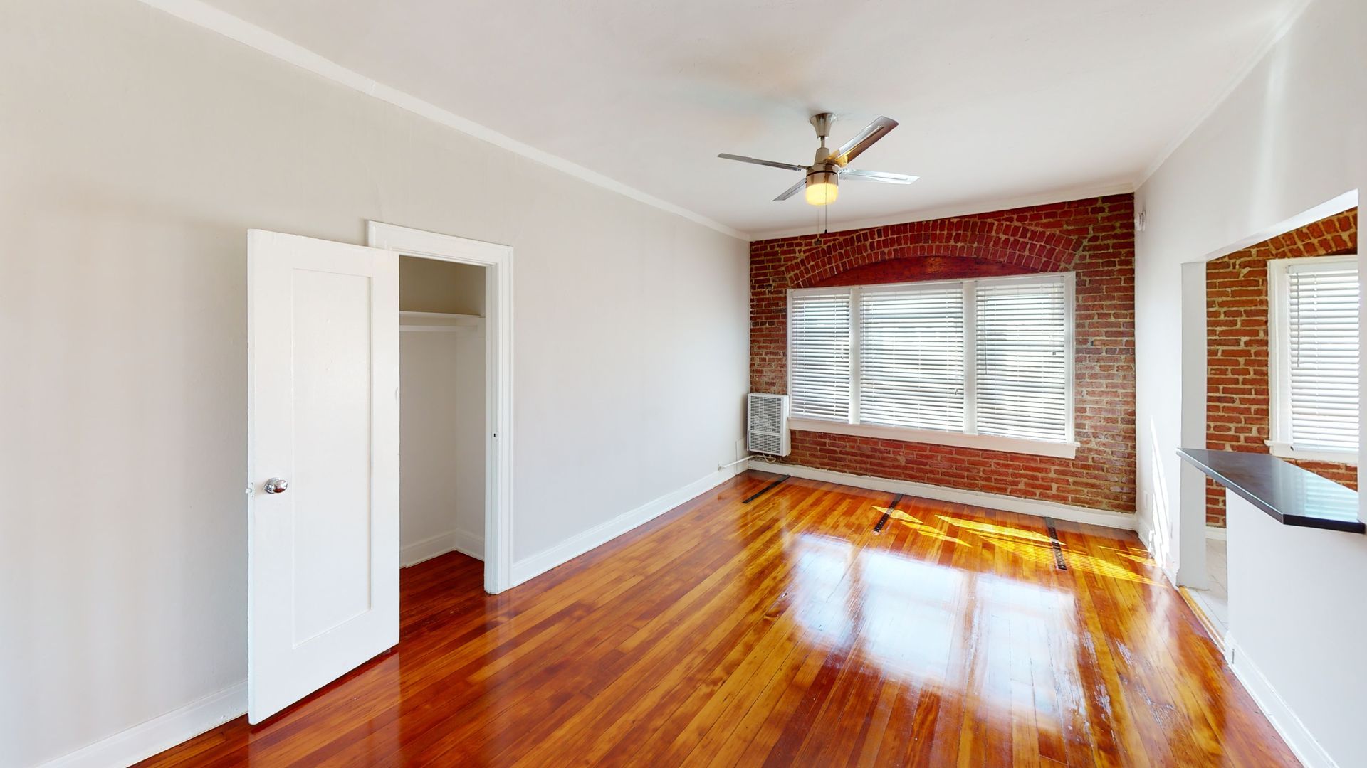 Empty room with hardwood floors, exposed brick wall with windows, white walls, and closet.
