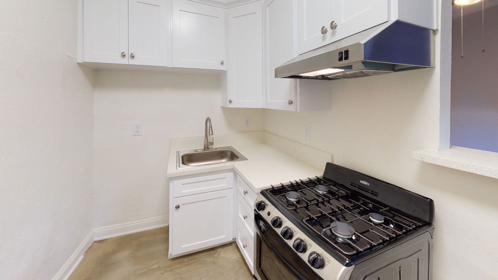 Small kitchen with white cabinets, stainless steel stove, and sink.