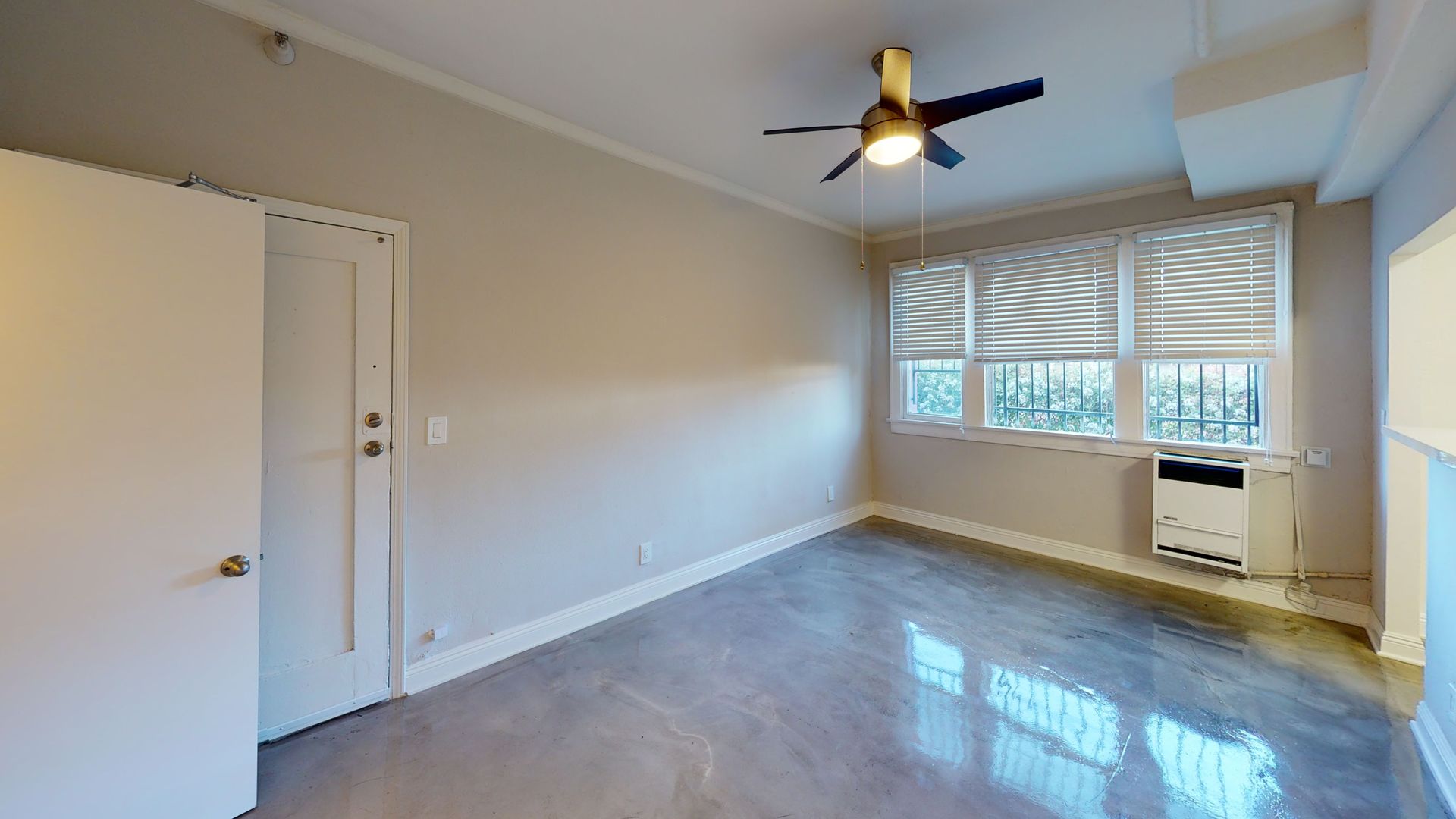 Empty room with concrete floor, white walls, closed door, window with blinds, ceiling fan.