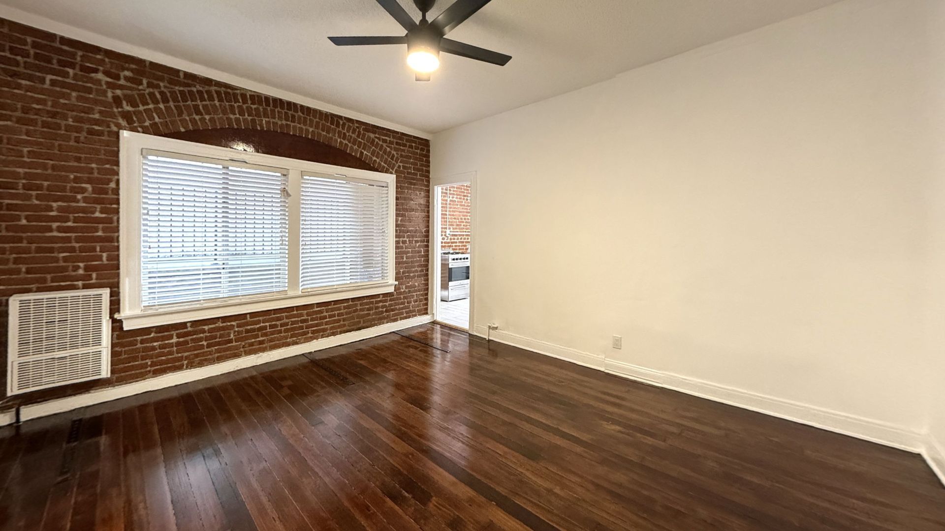 Empty room with brick accent wall, large window, and dark wood floors.