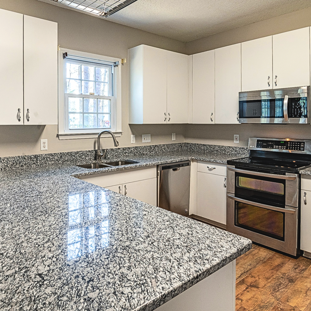 A kitchen with granite counter tops , stainless steel appliances , and white cabinets.