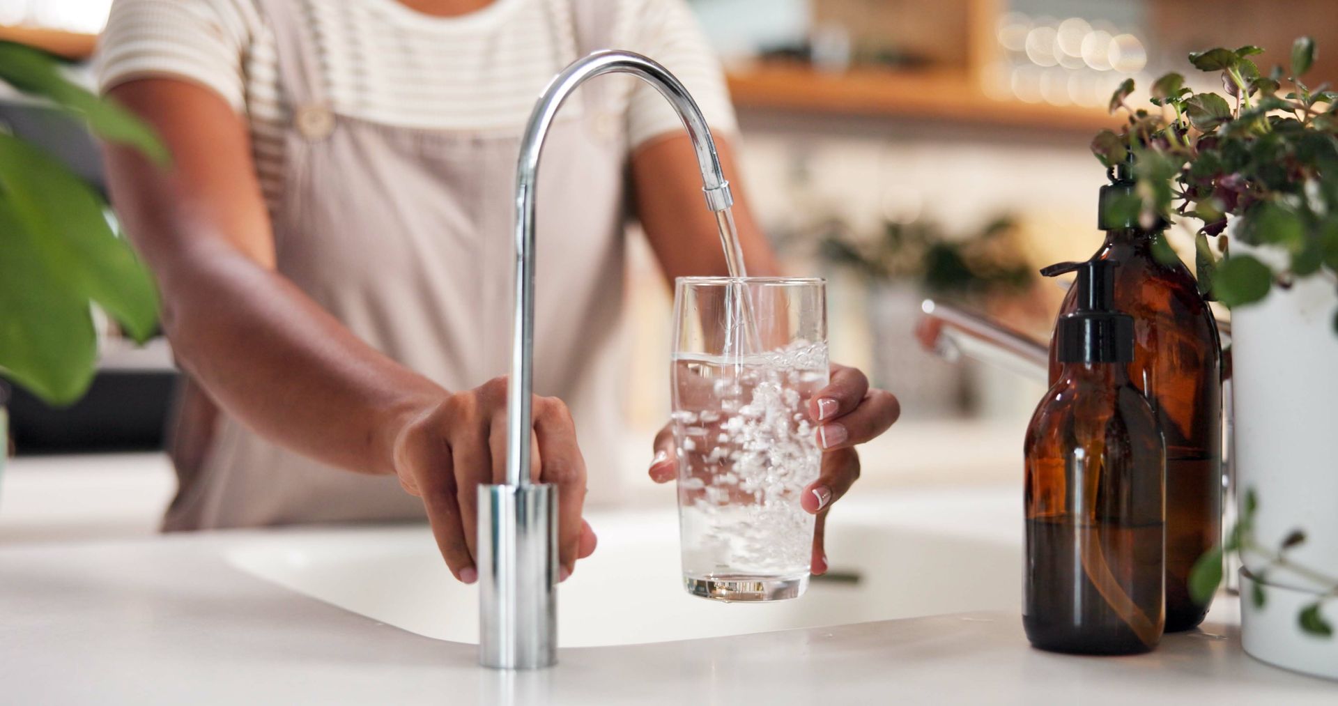 Person filling a clear glass with water from a modern kitchen faucet.