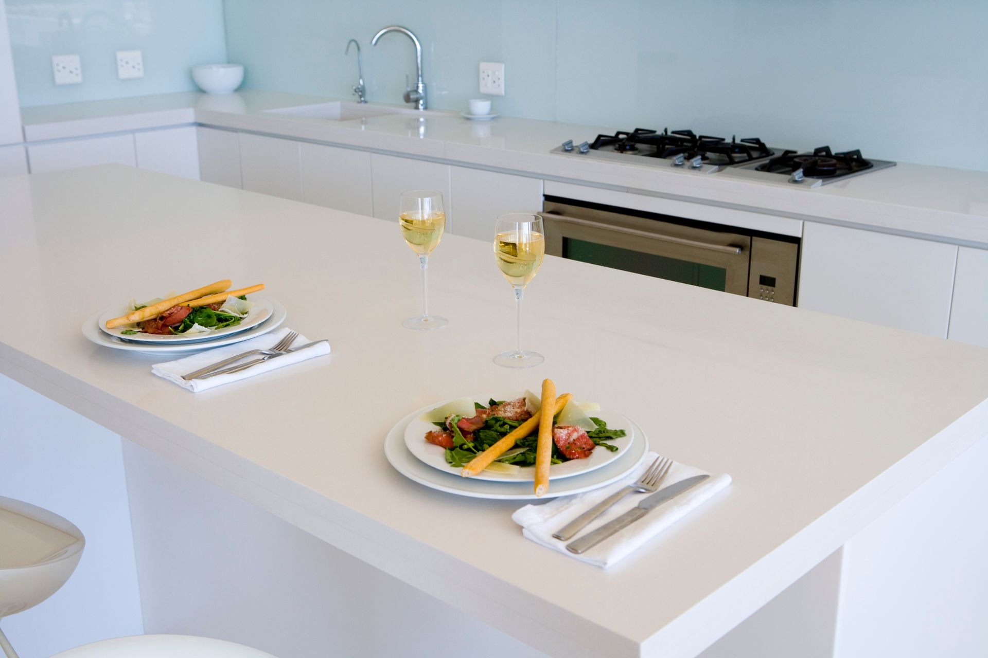 Kitchen with white counters and countertops. The kitchen island has plates of food and drinks.
