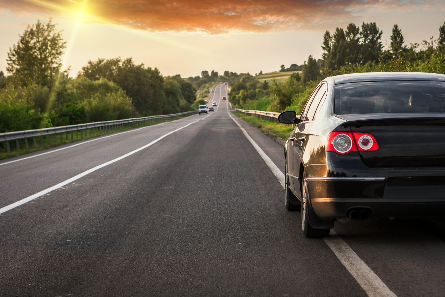 Black car parked on the side of an empty asphalt road at sunset.