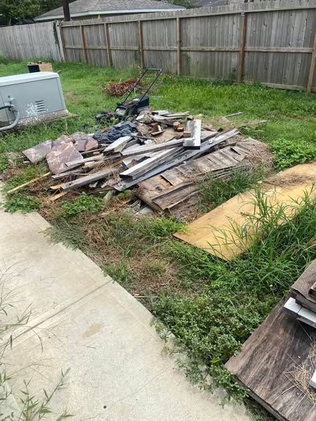 A pile of wood is sitting in the grass next to a sidewalk.