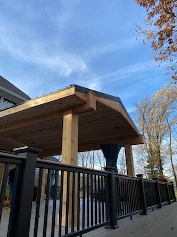 A wooden deck with a black railing and a wooden roof.