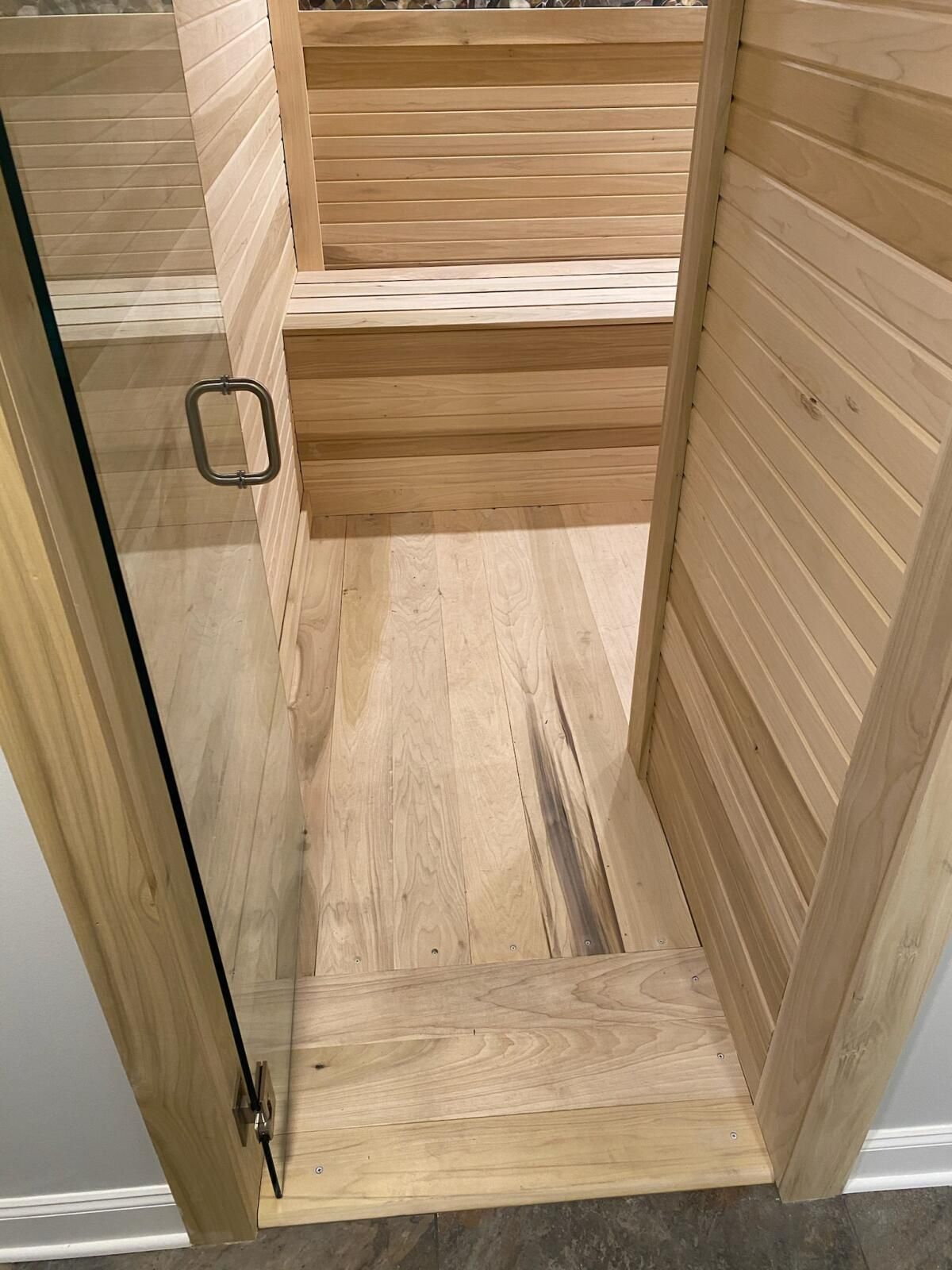 A doorway leading to a wooden sauna with a glass door.