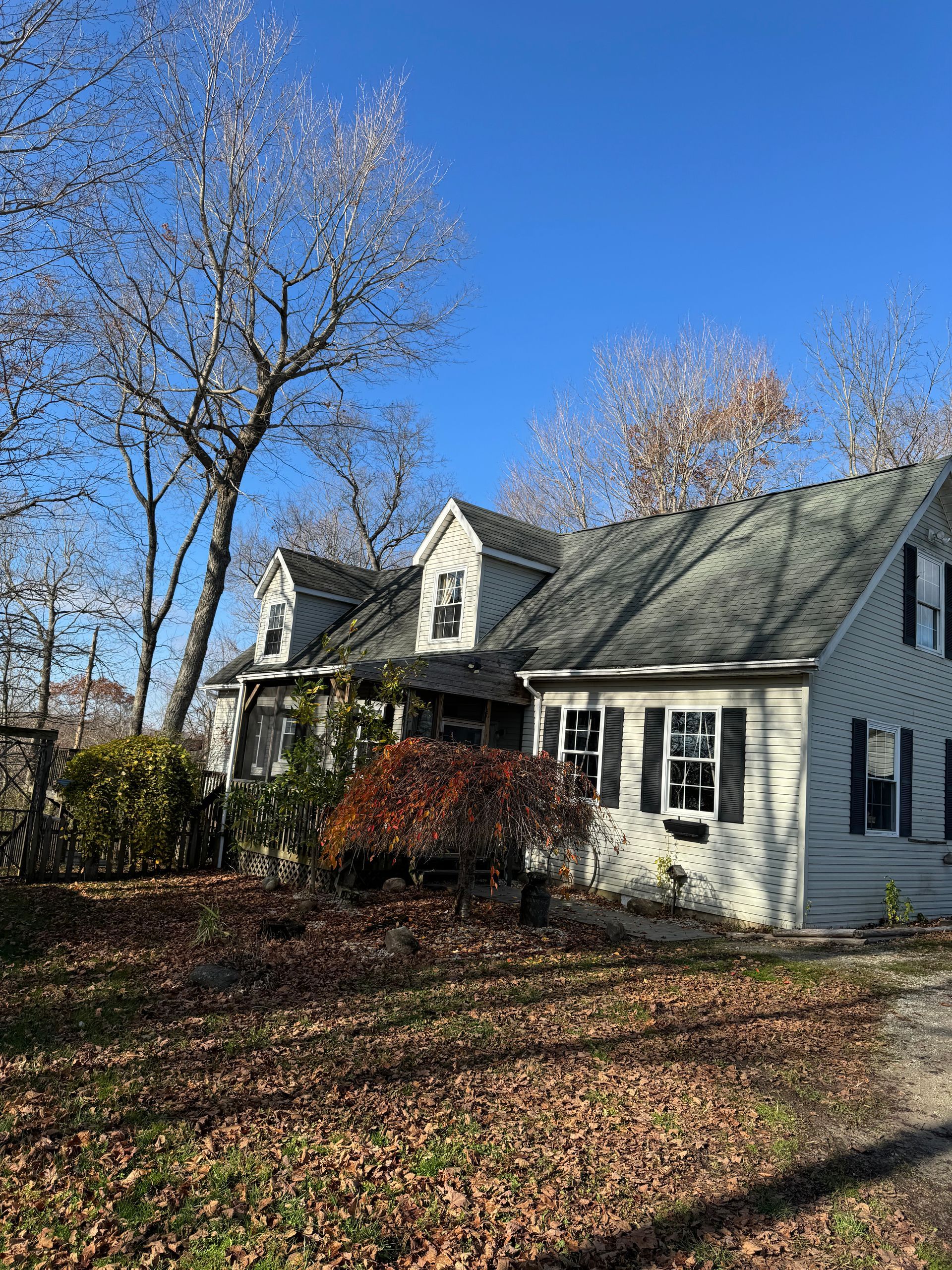 House with gray siding and black shutters, two dormers, and bare trees in autumn.