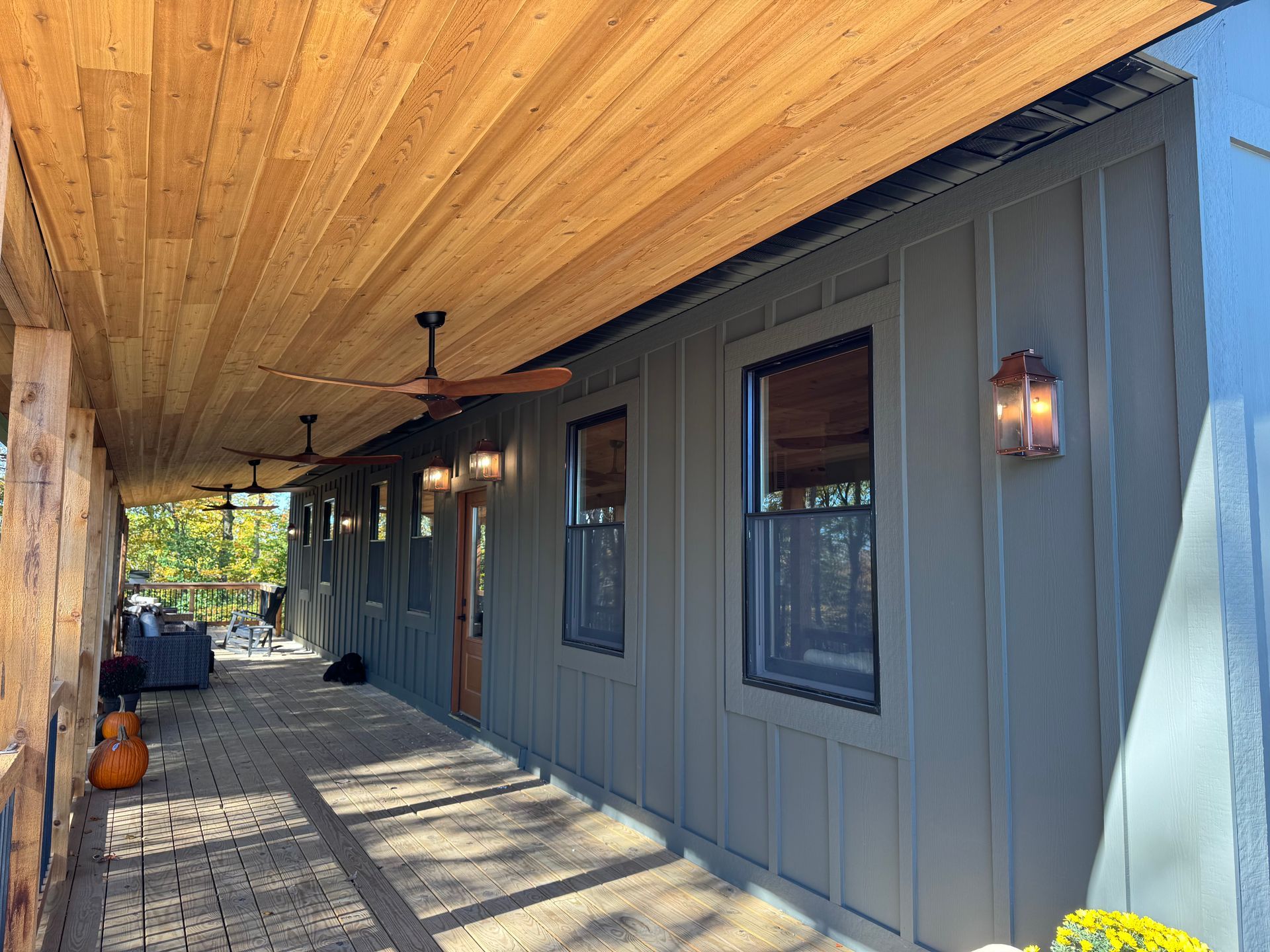 Covered porch with wood ceiling and green siding. Windows, fans, and sconces line the wall.