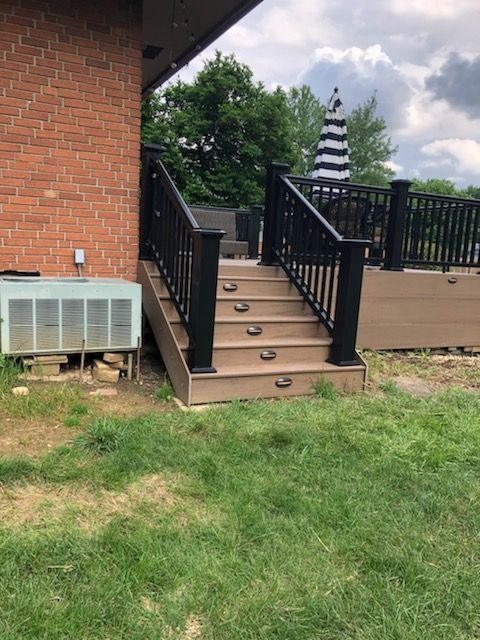 A deck with stairs and a black railing next to a brick house.