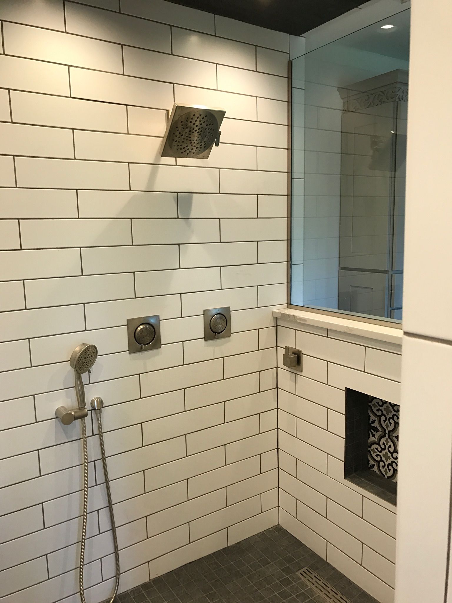 A bathroom with white tiles and a shower head.