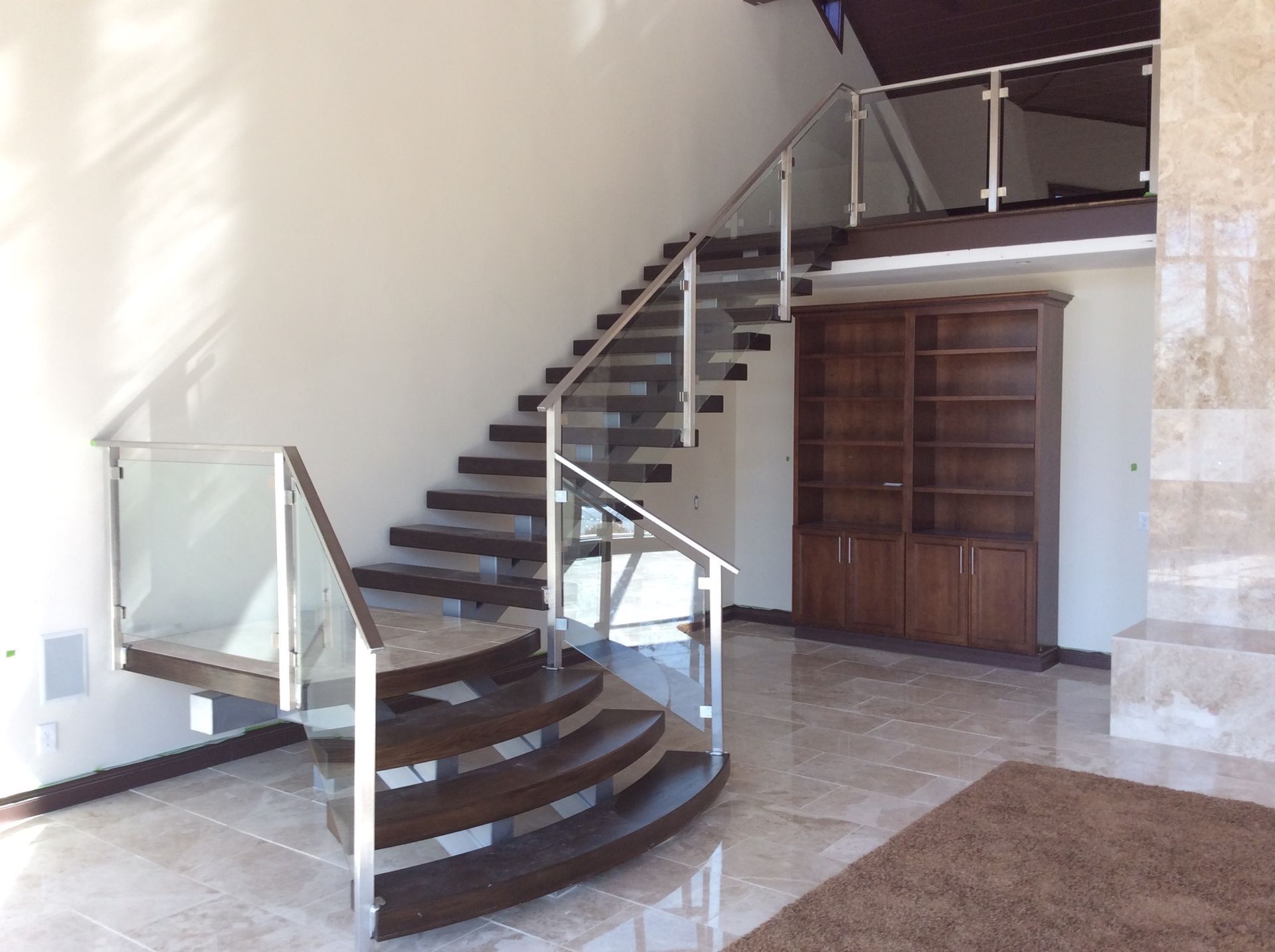 A curved staircase with a glass railing in an empty room.