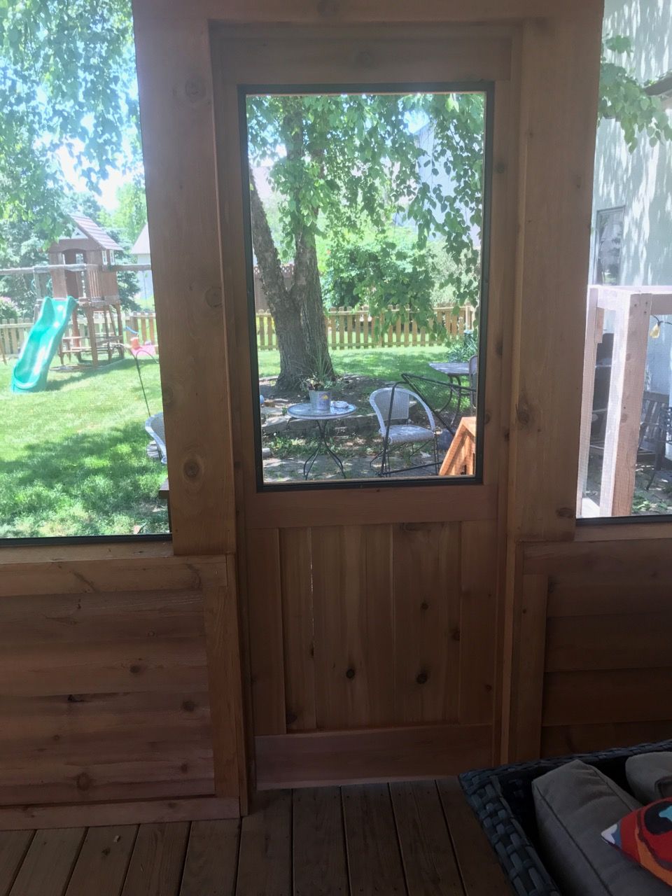A screened in porch with a view of a backyard through a window.