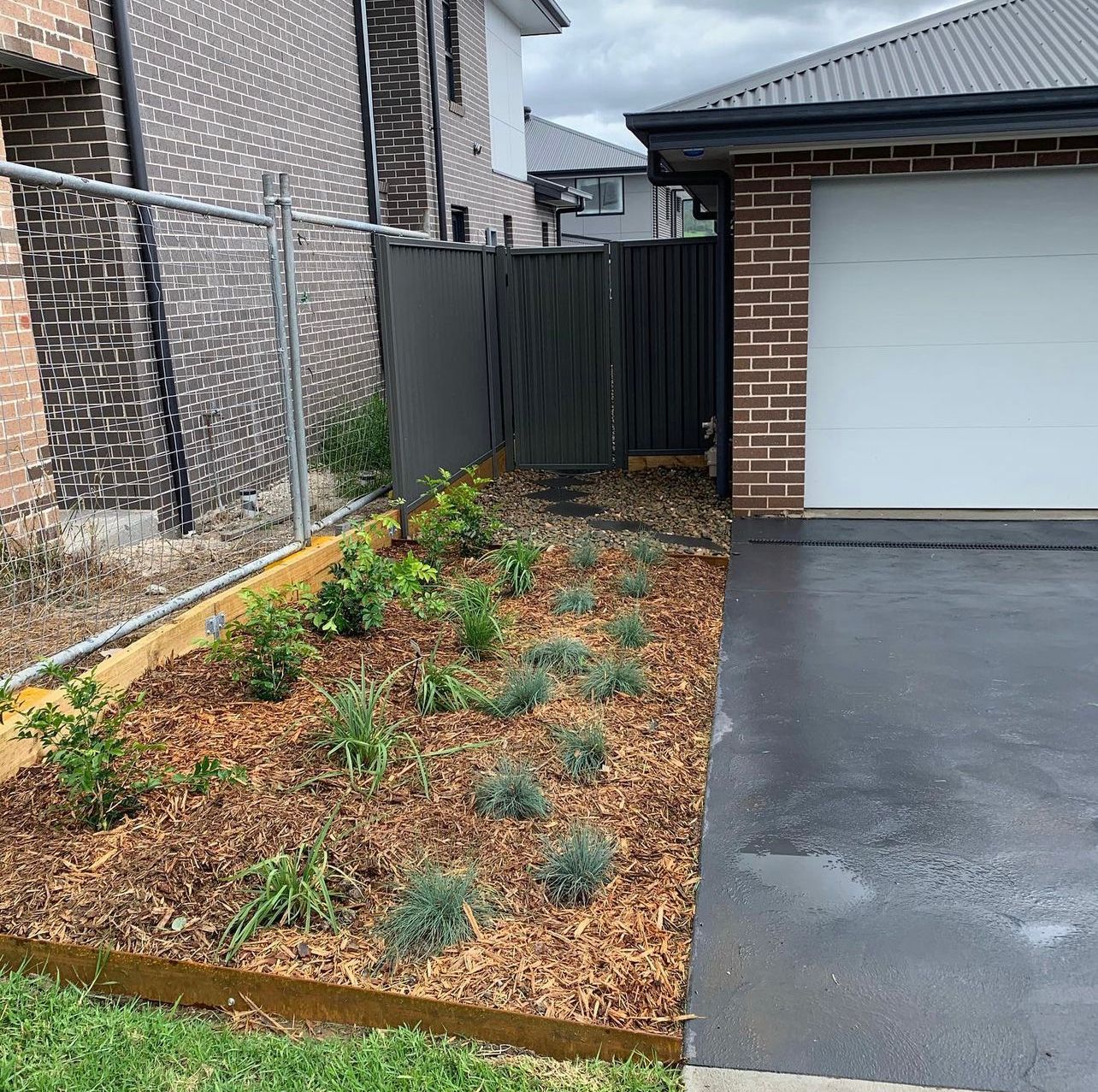 A Brick House With a White Garage Door and a Garden in Front of It — Illawarra Gardening Landscapes in Shellharbour, NSW