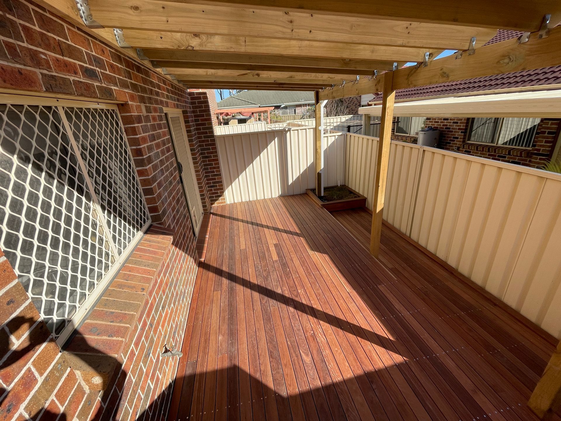 A Wooden Deck With a Brick Wall and a White Fence — Illawarra Gardening Landscapes in Shellharbour, NSW