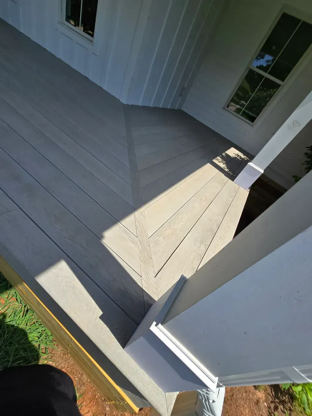 A wooden porch deck with diagonal boards meeting at a seam, featuring a white support post and a window on the wall.