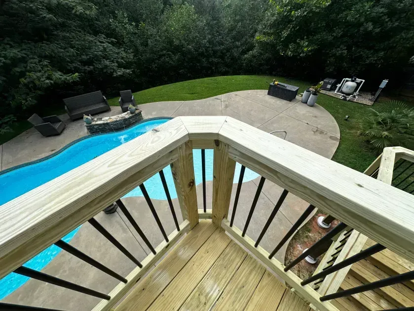 High-angle view of a wooden deck railing overlooking a backyard with a swimming pool and patio furniture.