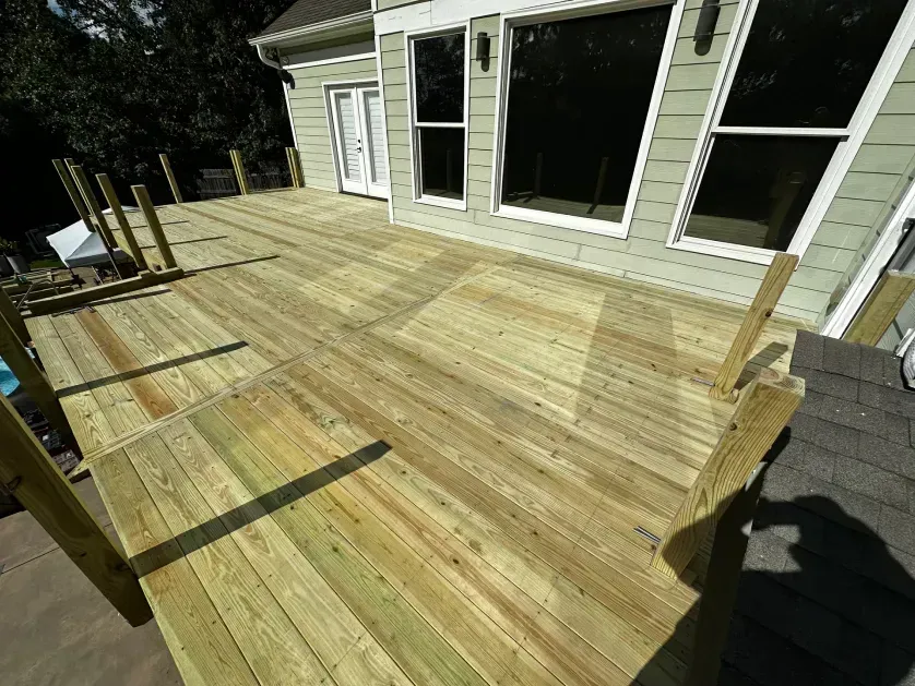A high-angle view of a newly constructed wooden deck attached to the back of a light green house.