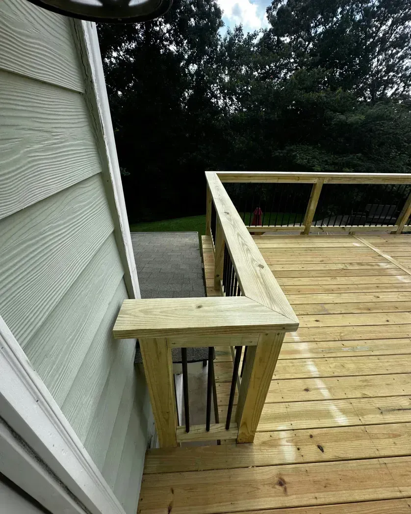 A newly built wooden deck railing section attached to the side of a light green house with black metal balusters.