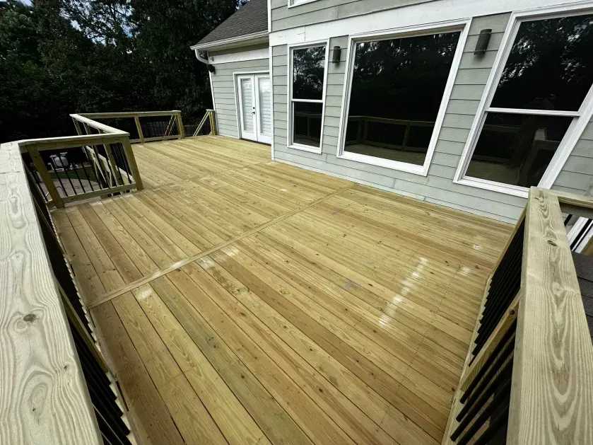A newly built wooden deck attached to the rear of a two-story gray house with large glass windows.
