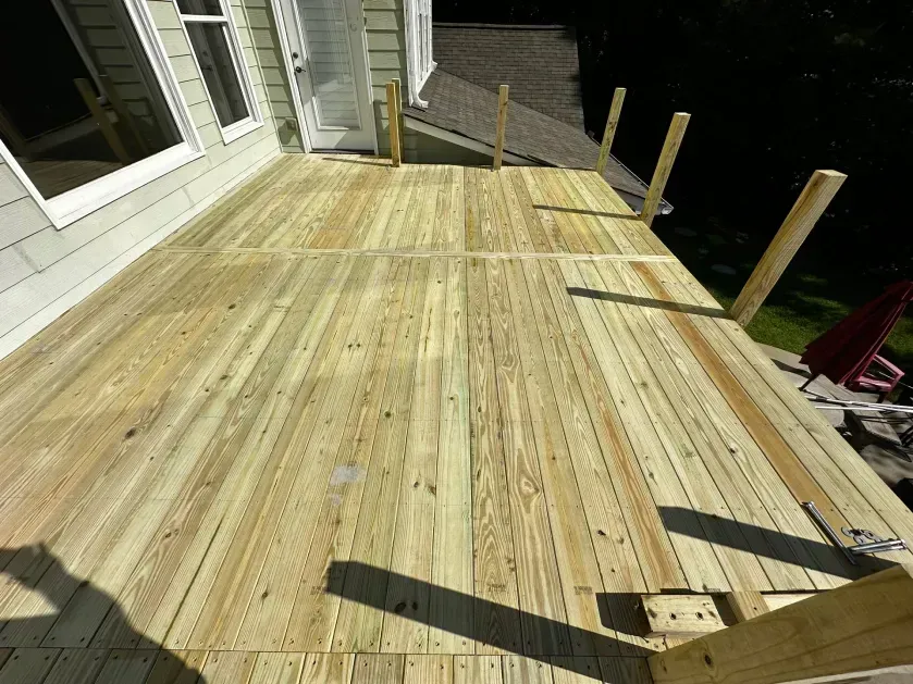 A freshly built wooden deck attached to the side of a house, featuring vertical posts ready for railing installation.