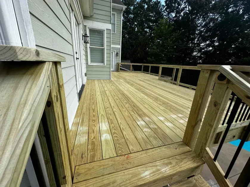 A freshly built wooden deck with light-colored boards, railings, and steps extending from the side of a grey house.