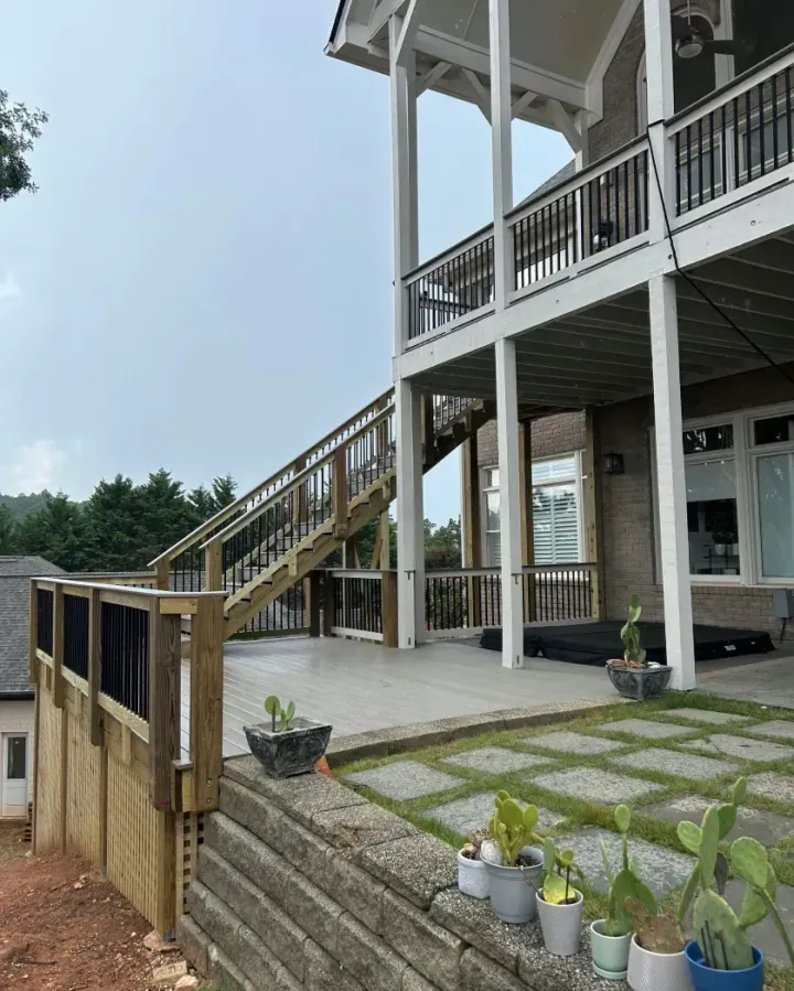 A multi-story house with a white exterior, featuring a wooden staircase descending to a stone patio with potted plants.