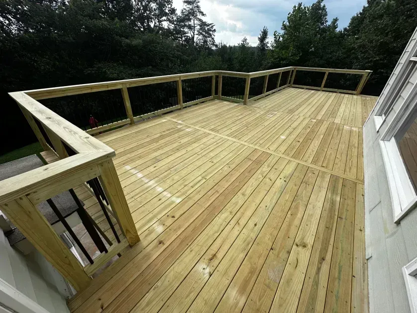 A high-angle view of a newly built light-colored wooden deck with wooden railings, overlooking a forest.