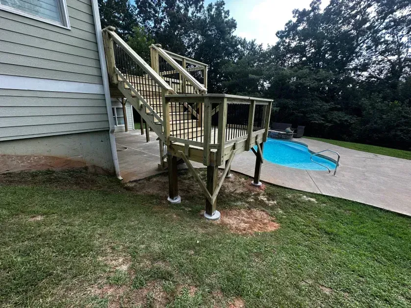 A wooden deck with stairs attached to a house exterior, overlooking a backyard swimming pool.