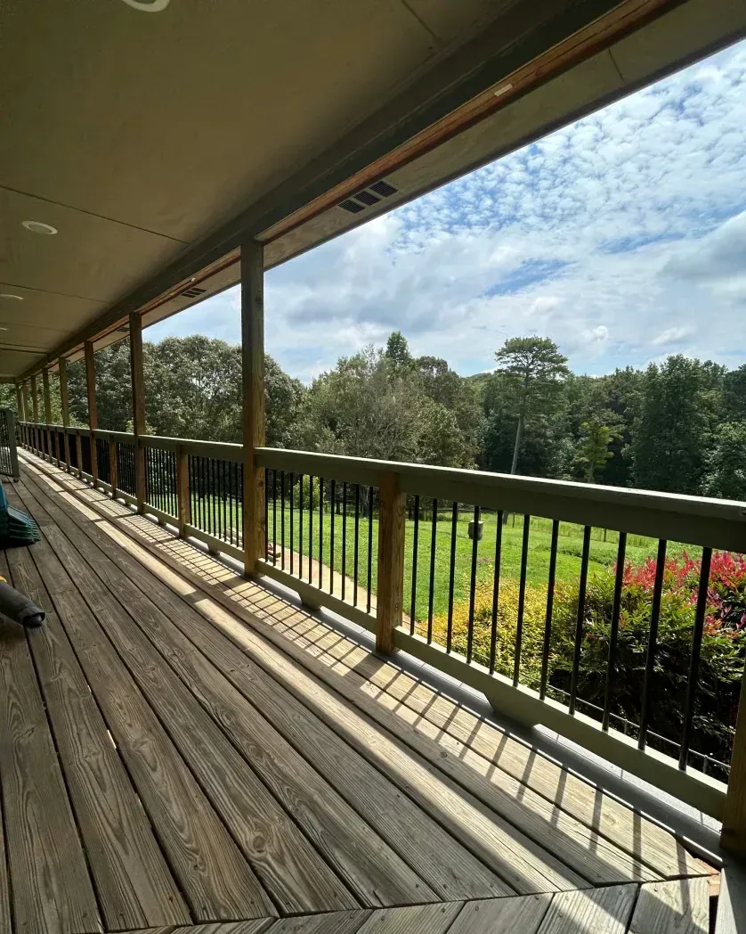 A wooden deck overlooking a lush green lawn and trees under a partly cloudy sky.