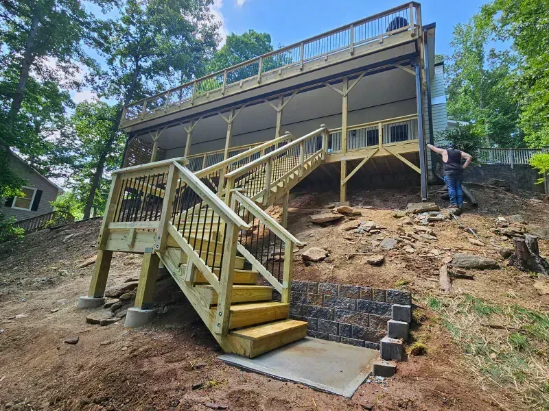 New wooden staircase with railings leading from a sloped, rocky yard up to a raised deck on the back of a house.