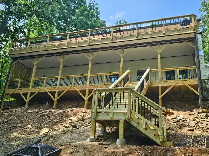 A two-story wooden deck with railings on a house exterior, featuring a set of stairs leading to the ground.