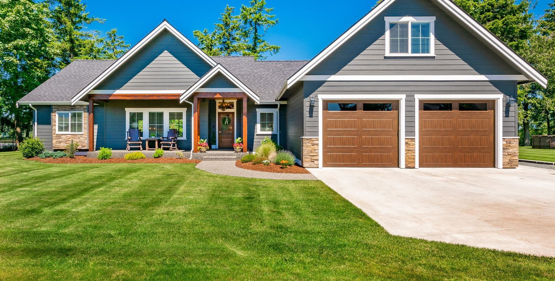 Gray craftsman-style home with brown garage doors, lawn, and blue siding.