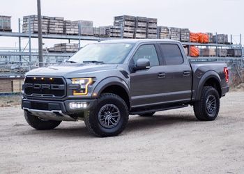 A ford raptor is parked in a gravel lot in front of a warehouse.