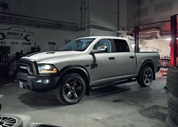 A silver dodge ram truck is parked in a garage next to a pile of tires.