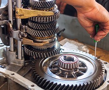 A person is working on a gearbox with a screwdriver.