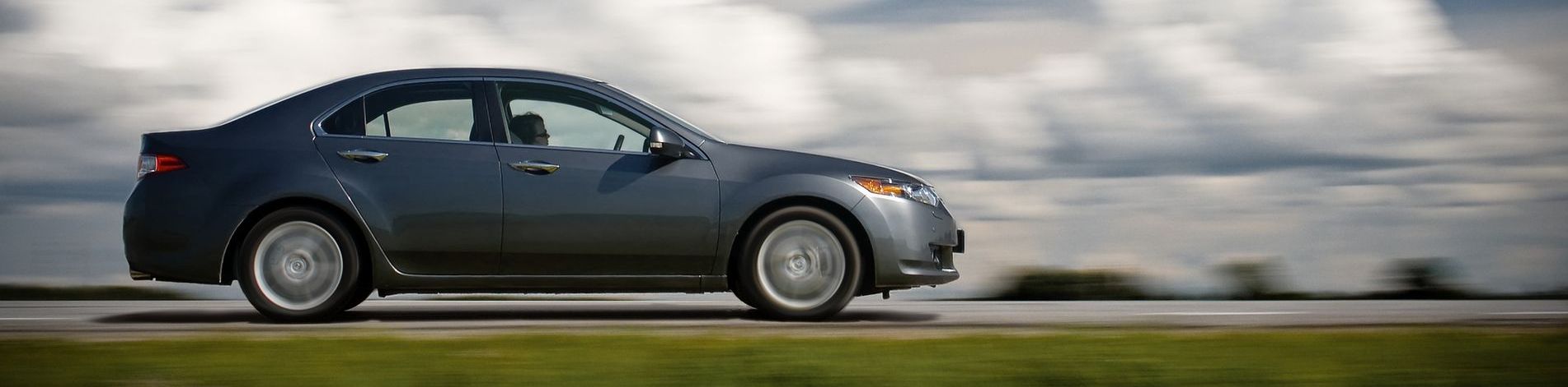 A car is driving down a road with a cloudy sky in the background.