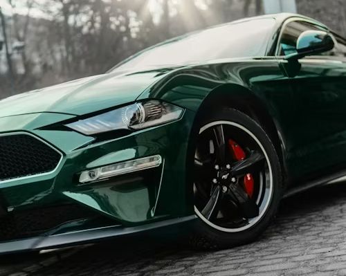 Black Ford Mustang parked outdoors, lit by warm sunlight.