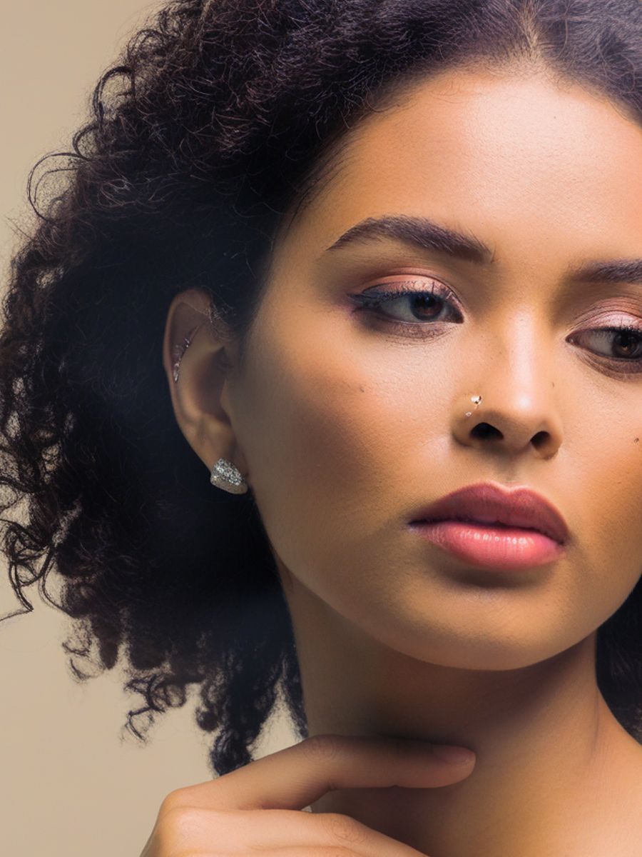Young woman with curly hair, light skin, wearing earrings, gazing to the side, touching her chin.