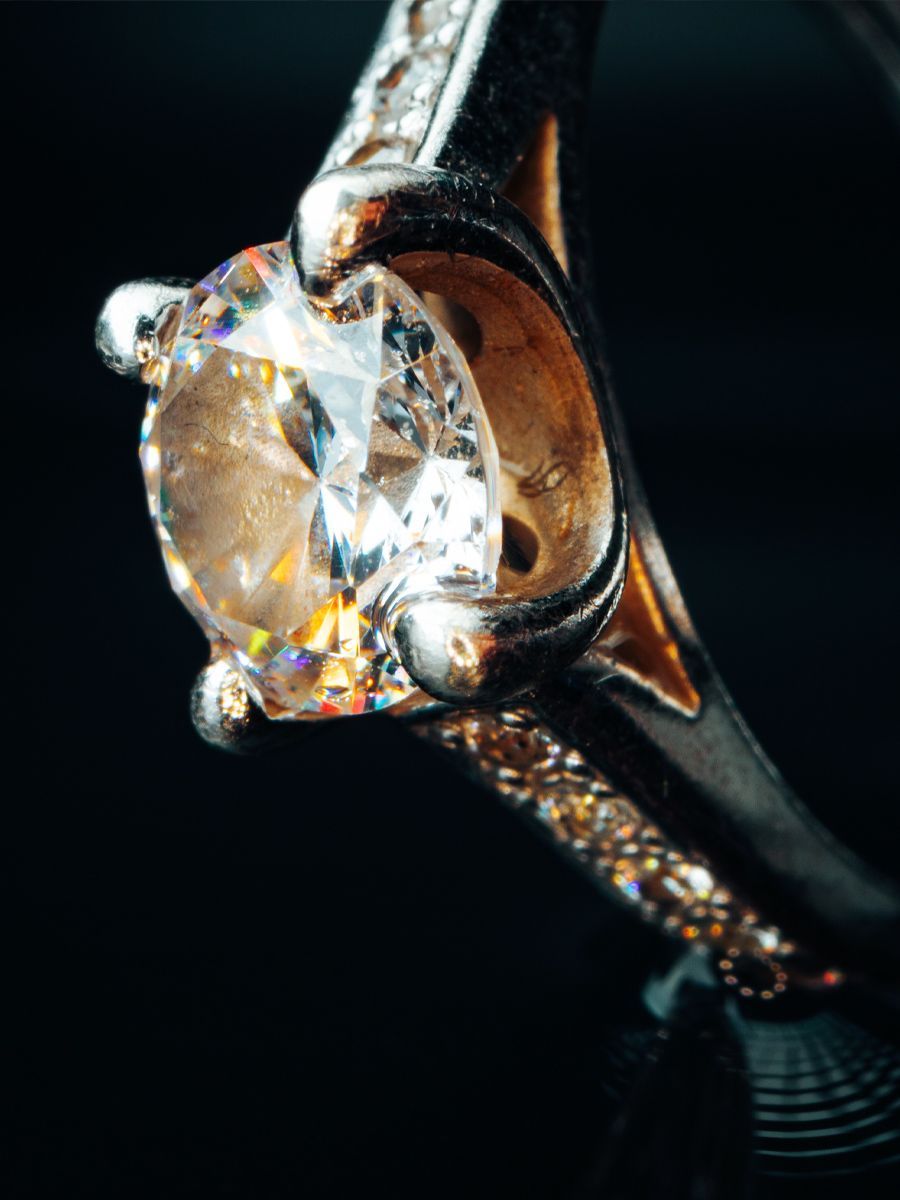 Diamond engagement ring, close-up with a large, round diamond and smaller accent diamonds on a dark background.