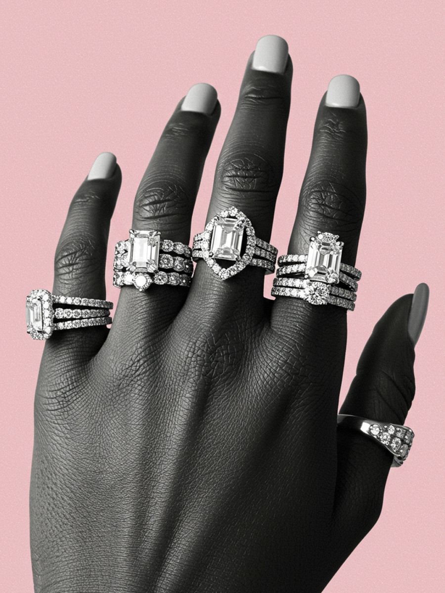 Black and white photo of a hand adorned with multiple diamond rings on a pink background.