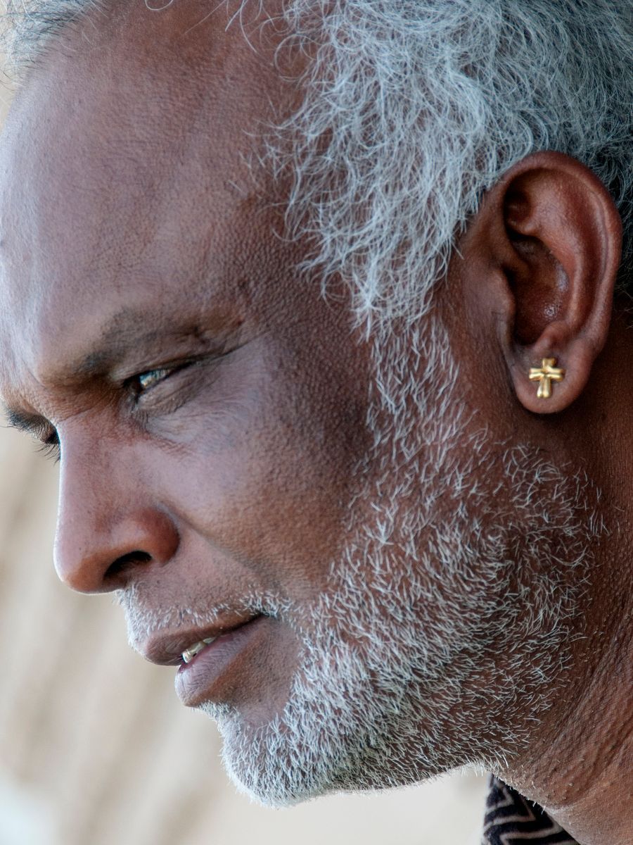 Man with graying hair and beard, wearing a gold cross earring, looking down thoughtfully.