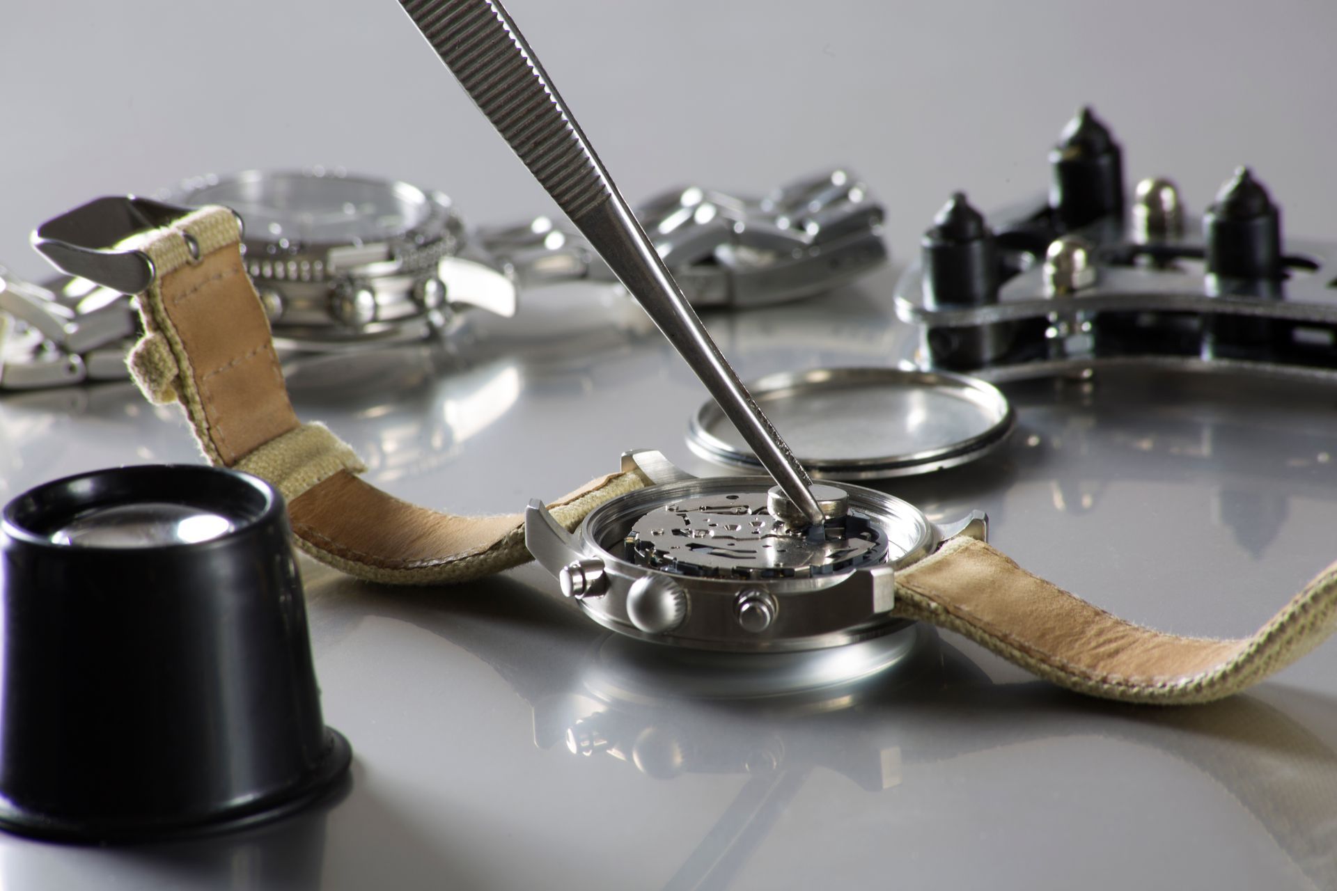 Watch being repaired with tweezers, close-up. Tools and parts on a reflective surface.