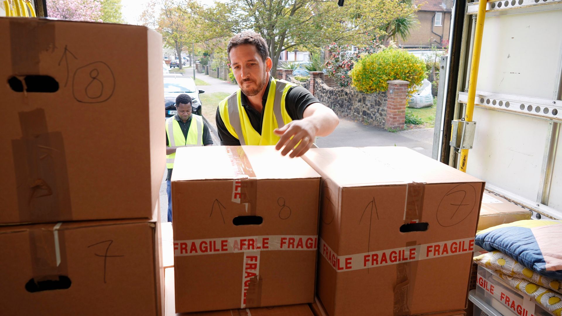 A man in a yellow vest is loading boxes into a truck.