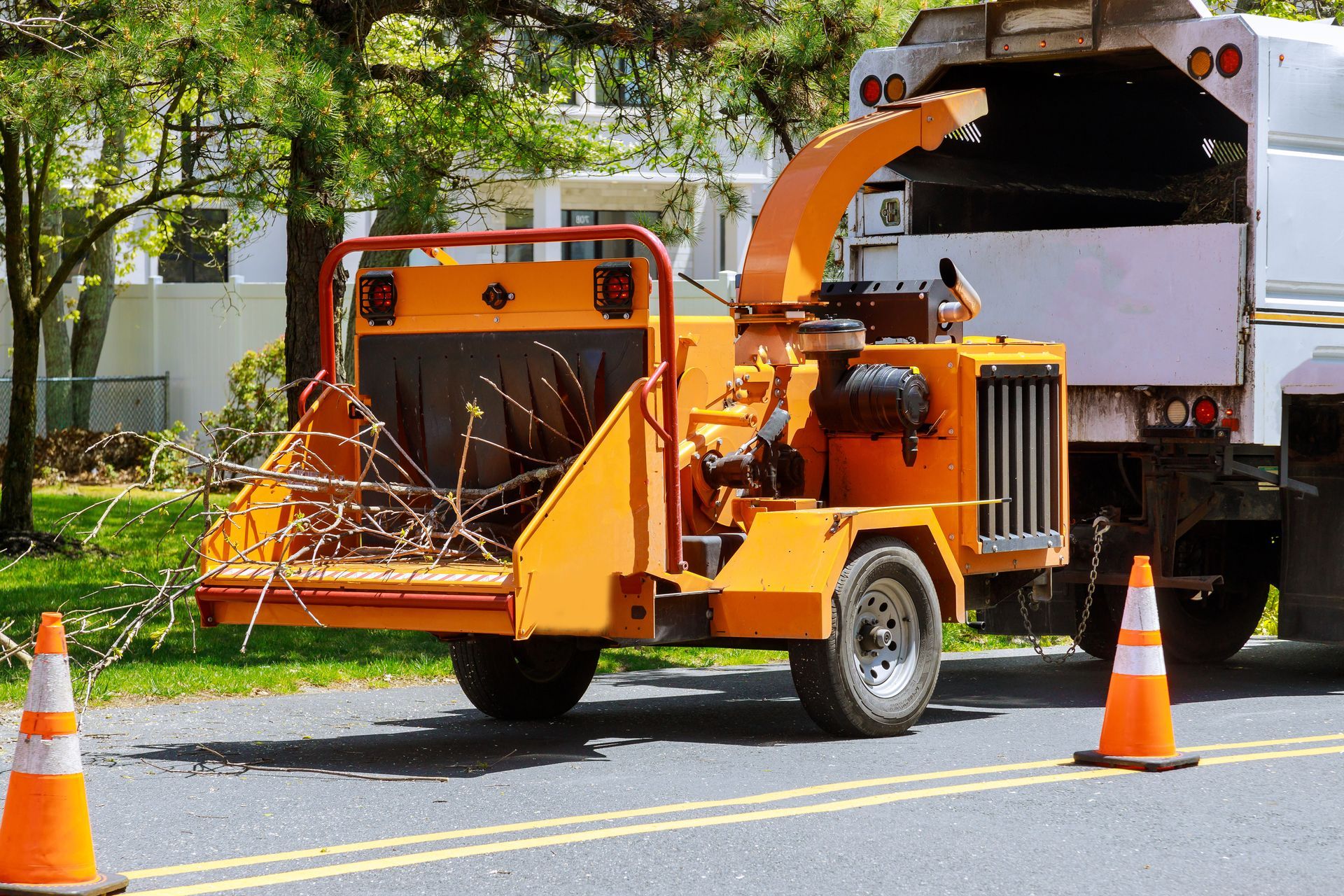 A tree chipper is parked on the side of the road next to traffic cones.
