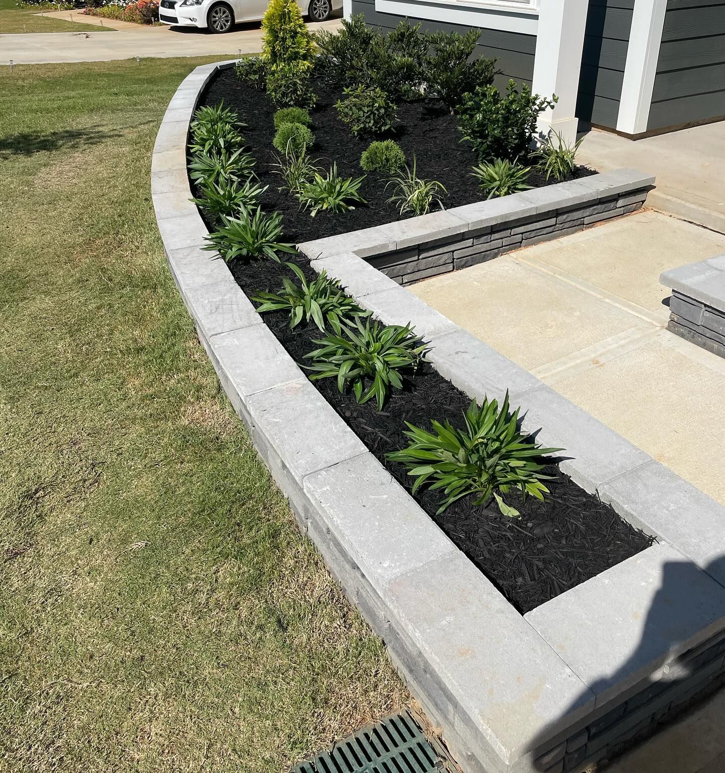 Gray stone retaining wall with a black mulch flower bed in front of a house.
