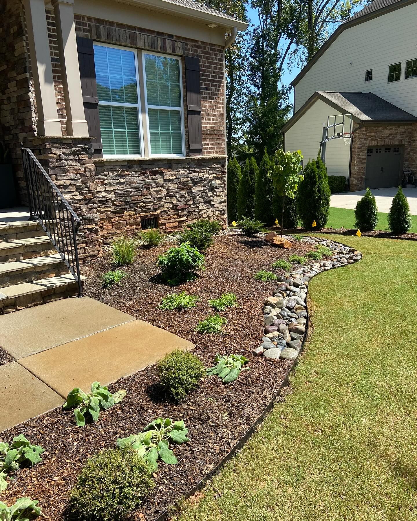 Landscaped yard with brown mulch, stones, green plants, and a stone house.