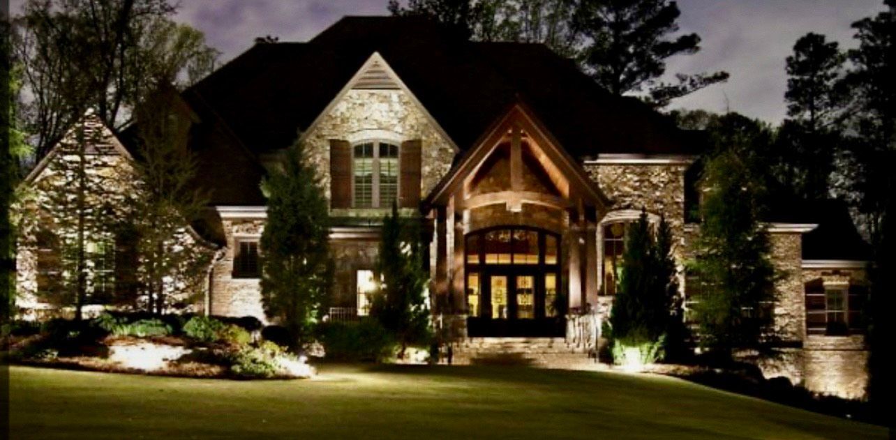Night view of a large stone house illuminated by outdoor lighting.